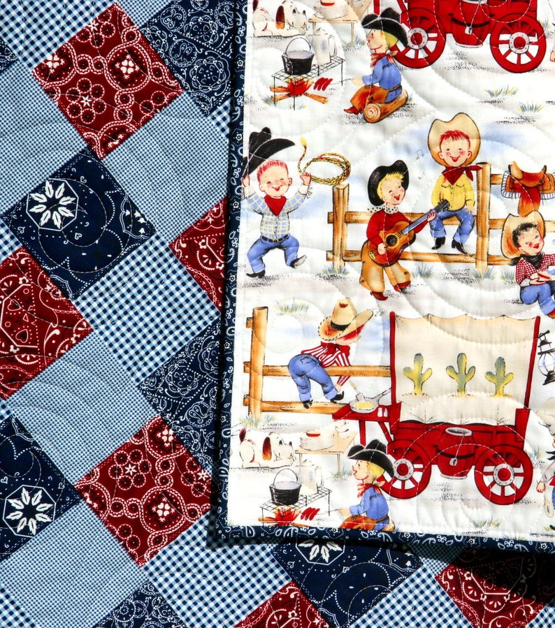 May include: A white and blue patchwork quilt with a red, white, and blue bandana print. The quilt features a scene of cowboys and a wagon on a white background.
