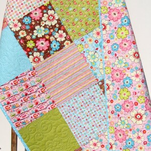 May include: A patchwork baby quilt with a variety of colorful floral and owl prints. The quilt is edged with a blue and white polka dot trim.