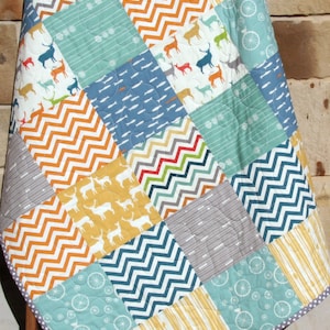 May include: A patchwork quilt with a variety of patterns, including chevron, stripes, and deer silhouettes. The quilt is made in shades of blue, yellow, orange, and gray.