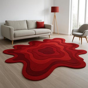 Pode incluir: Um tapete vermelho único com um design orgânico em camadas. O tapete apresenta diferentes tons de vermelho, criando um efeito dimensional. Está colocado sobre um chão de madeira clara, complementando a decoração interior moderna.