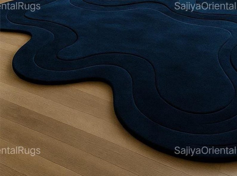Modern deep blue irregular-shaped wool rug with abstract wavy edges, styled in a contemporary living room with a beige sofa, light wood flooring, and neutral decor.