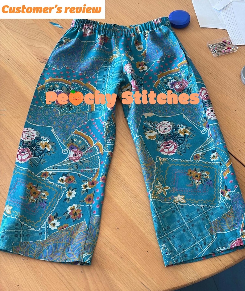 K&ouml;nnte beinhalten: T&uuml;rkisfarbene Hose mit elastischem Bund und einem sich wiederholenden Muster aus Blumenarrangements und f&auml;cherf&ouml;rmigen Motiven in Rosa, Wei&szlig; und Gelb. Der Text "Customer's review" und "Peachy Stitches" ist &uuml;ber das Bild gelegt.