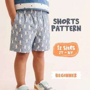 Op de afbeelding: Lichtblauwe shorts met een patroon van witte zeemeeuwen. De shorts hebben een elastische tailleband en zakken. De tekst "SHORTS PATTERN", "12 Sizes 2T-16Y" en "BEGINNER" is ook zichtbaar.