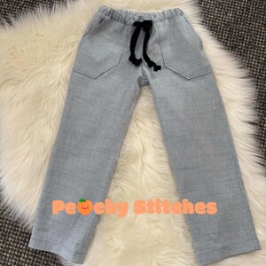 Op de afbeelding: Lichtblauwe broek met een subtiel ruitpatroon, voorzien van een elastische tailleband met een zwart trekkoord, twee voorzakken en een rechte pijp. De tekst "Customer's review" en "Peachy Stitches" met een perzik-icoon zijn zichtbaar.