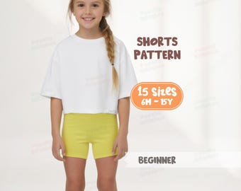 May include: A young girl wearing a white crop top and yellow shorts. The image includes text that reads "SHORTS PATTERN", "15 Sizes 6M - 15Y", and "BEGINNER".