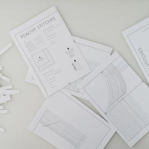 May include: A collection of white sewing pattern sheets with the text "PEACHY STITCHES" and detailed diagrams. A pile of white paper strips is on the left. The patterns appear to be for sewing projects.