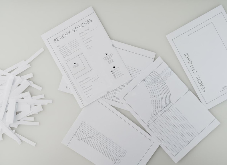 May include: A collection of white sewing pattern sheets with the text "PEACHY STITCHES" and detailed diagrams. A pile of white paper strips is on the left. The patterns appear to be for sewing projects.