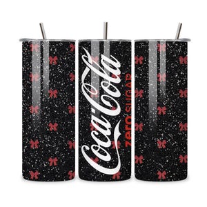 Könnte beinhalten: Ein schwarzer Glitzerbecher mit roten Schleifenakzenten und dem Coca-Cola Zero Sugar-Logo in Weiß. Der Becher enthält einen silbernen Strohhalm und Deckel. Ein festlicher Trinkartikel.