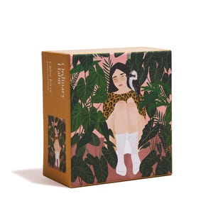 May include: A square box with a colorful illustration. The artwork depicts a person in a leopard print top, surrounded by lush green foliage, with a bird perched on their shoulder. The box has the text "Ordinary Habit" and the author's name.