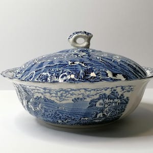 Op de afbeelding: Een blauwe en witte keramische serveerschaal met deksel. De schaal en het deksel hebben een landschapsontwerp. Het deksel heeft een kleine, decoratieve handgreep. De schaal is waarschijnlijk vintage of antiek.