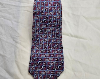 May include: A necktie featuring a repeating geometric pattern of interlocking silver-toned horse bits and stirrups arranged in a zigzag formation. The design is set against a deep burgundy background with light blue accents throughout the fabric.