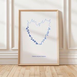 Puede incluir: Impresión artística enmarcada con un marco de madera clara. La impresión presenta una forma de corazón azul formada por la palabra "amour" en cursiva. La frase francesa "L'amour est pour toujours" está impresa debajo.