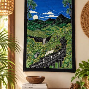 Puede incluir: Un tapiz rectangular de tela que presenta una ilustración detallada estilo batik de un tren cruzando un puente de piedra a través de un paisaje verde exuberante con montañas, árboles y una cascada bajo un cielo azul brillante.
