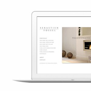 May include: A laptop computer displaying a website for interior designer Sebastien Fossel. The website features a white background with black text and a photo of a modern living room with a fireplace and a clear plastic chair. The text on the website reads "Transforming Spaces into Homes".