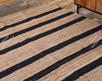 May include: A rectangular area rug featuring a woven natural tan jute texture with bold, parallel black stripes running diagonally across the surface. The rug displays a coarse, organic fiber construction with a consistent pattern throughout the piece.
