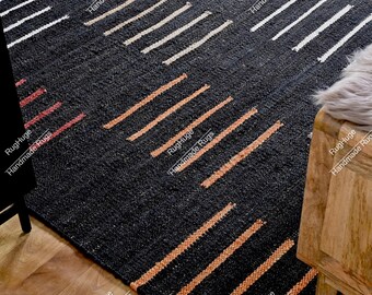 May include: A dark charcoal area rug featuring a repeating pattern of short, horizontal lines in white and muted orange. The rug has a textured, woven appearance with the text RugHuge Handmade Rugs repeated across the surface of the fabric.