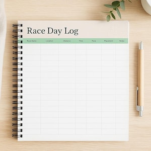 以下が含まれることがあります： 「Race Day Log」のタイトルが上部に印刷された、スパイラル綴じのノート。ノートにはレースの詳細を記録するためのグリッドレイアウトがあります。木製のペンがノートの右側に置かれ、背景には小さな植物が見えます。