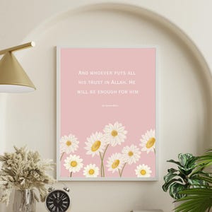 May include: A framed print with a pink background and white text that reads, "And WHOEVER PUTS ALL HIS TRUST IN ALLAH, HE WILL BE ENOUGH FOR HIM." The bottom of the print features a row of white daisies with yellow centers. The print is displayed on a wall.