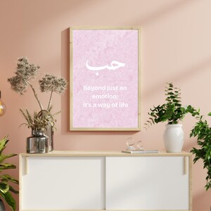 May include: A framed pink print with Arabic calligraphy and the text "Beyond just an emotion: It's a way of life." The print is displayed on a white cabinet with plants and decorative lighting.