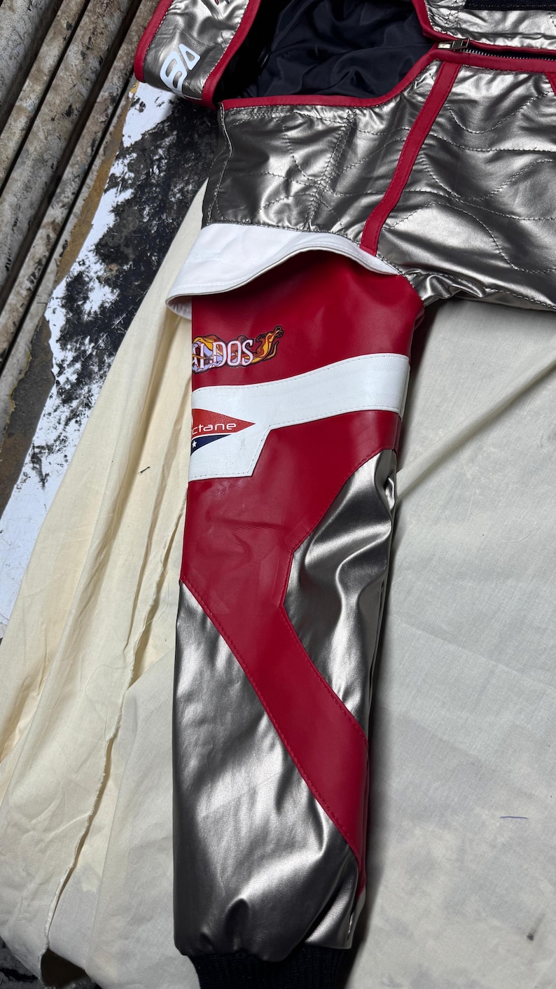 May include: Silver and red racing jacket with white accents. The jacket features a quilted design and a black collar. The sleeve has the text "DOS" and "ctane".