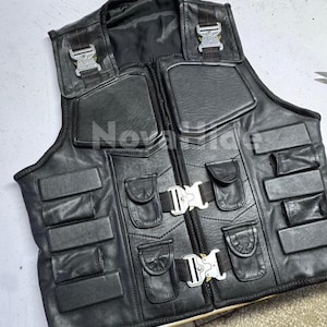 Puede incluir: Un chaleco t&aacute;ctico de cuero negro con m&uacute;ltiples paneles acolchados rectangulares, cuatro bolsillos peque&ntilde;os con solapa y dos hebillas met&aacute;licas plateadas de liberaci&oacute;n r&aacute;pida en el frente. La palabra NovaHide est&aacute; impresa en blanco en el centro.
