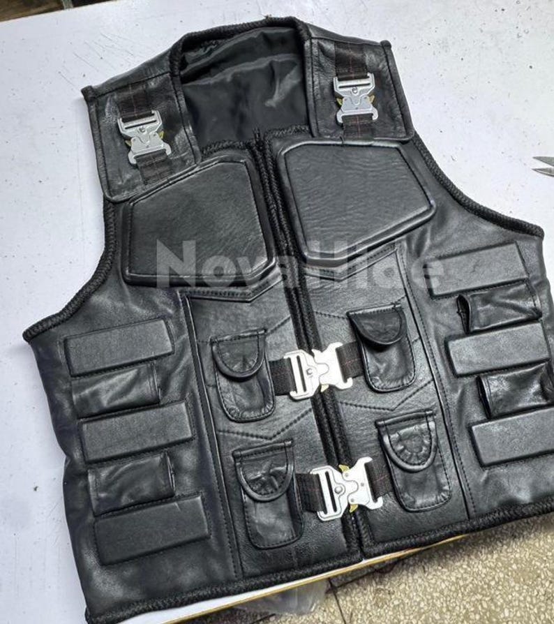 Puede incluir: Un chaleco t&aacute;ctico de cuero negro con m&uacute;ltiples paneles acolchados rectangulares, cuatro bolsillos peque&ntilde;os con solapa y dos hebillas met&aacute;licas plateadas de liberaci&oacute;n r&aacute;pida en el frente. La palabra NovaHide est&aacute; impresa en blanco en el centro.