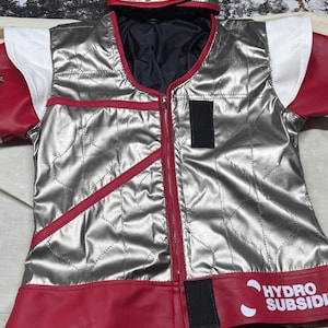 May include: Silver quilted vest with red trim and accents, featuring a full-length zipper. The vest has a matching hood and sleeves with white and red details. The text "HYDRO SUBSIDI" is visible on the bottom hem.