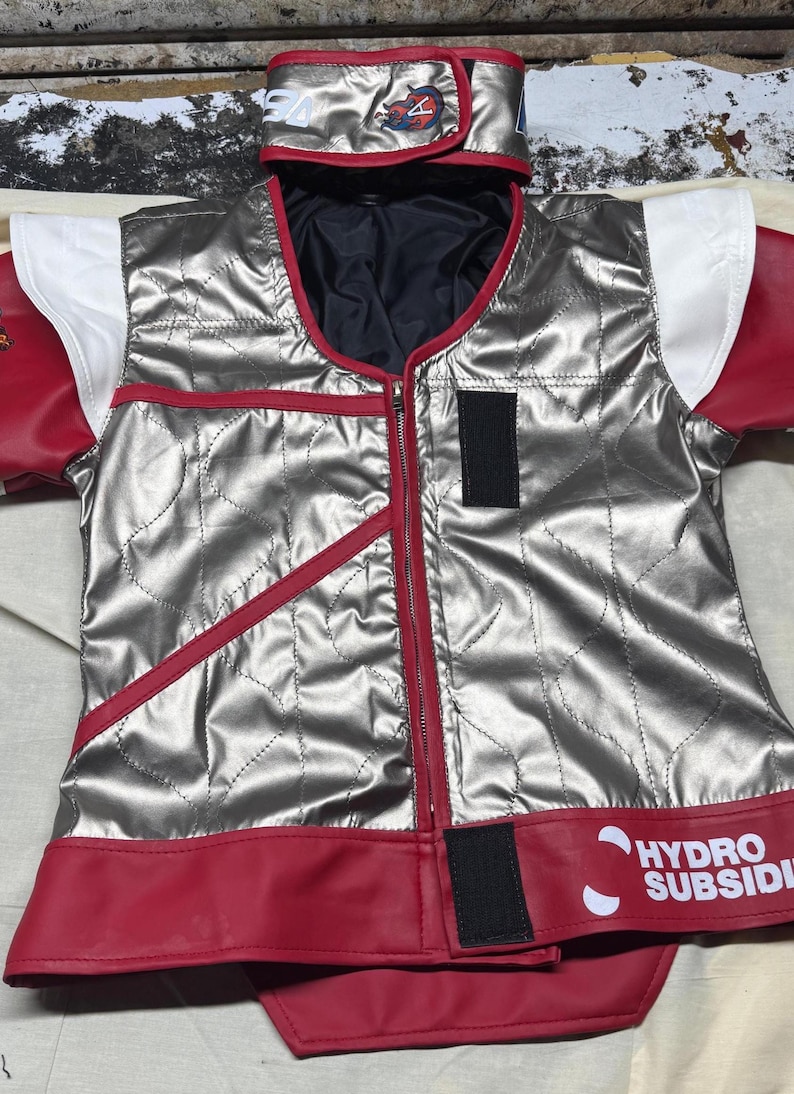 May include: Silver quilted vest with red trim and accents, featuring a full-length zipper. The vest has a matching hood and sleeves with white and red details. The text "HYDRO SUBSIDI" is visible on the bottom hem.