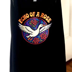 May include: Black tank top with a colorful graphic. The graphic features a white bird with outstretched wings, surrounded by red roses and the text "ECHO OF A ROSE" in gold lettering.