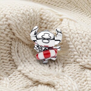 May include: A silver-toned charm shaped like a cartoon character with large ears, featuring a red and white striped life preserver ring around its waist. The charm has a polished, reflective metallic finish and detailed engraved facial features.
