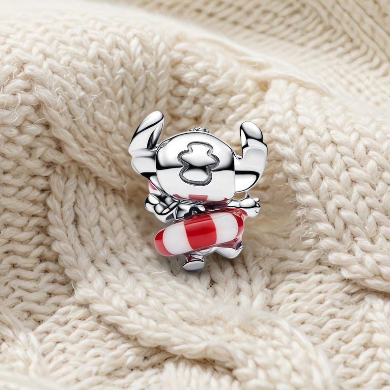 May include: A silver-toned charm shaped like a cartoon character with large ears, featuring a red and white striped life preserver ring around its waist. The charm has a polished, reflective metallic finish and detailed engraved facial features.