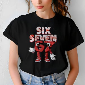 May include: Black t-shirt featuring the words "SIX SEVEN" in a distressed, brick-like font. Below the text is a cartoon character made of red bricks, resembling the numbers 67, with white gloves and shoes.