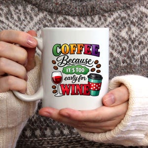 May include: White ceramic coffee mug with the text "COFFEE Because it's too early for WINE". The mug features a wine glass, coffee beans, and a to-go coffee cup with a red polka dot design.