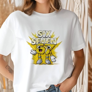 May include: White t-shirt featuring a cartoon graphic of the words "SIX SEVEN" in yellow, with the numbers designed as animated characters. The design includes a yellow burst background and cartoon details.