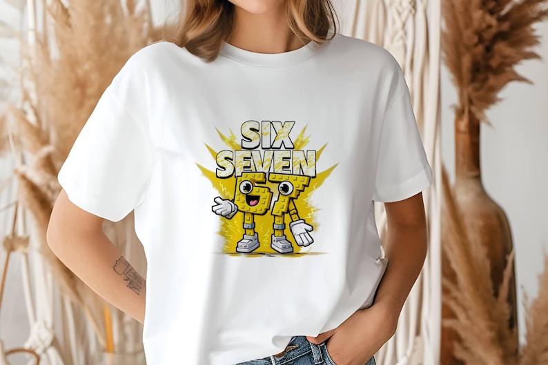 May include: White t-shirt featuring a cartoon graphic of the words "SIX SEVEN" in yellow, with the numbers designed as animated characters. The design includes a yellow burst background and cartoon details.