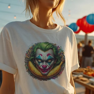 May include: White t-shirt featuring a colorful graphic of the Joker's face with green hair, red nose, and blue accents. The design includes a yellow banana. The shirt has rolled-up sleeves and a crew neck.