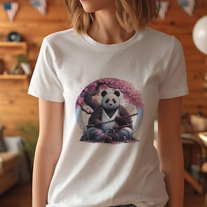 May include: White t-shirt featuring a panda dressed as a samurai, seated beneath a cherry blossom tree. The panda wears traditional armor and holds two swords. The design is set within a circular frame.