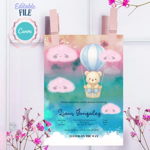 Puede incluir: Una tarjeta de invitación para baby shower con una ilustración en acuarela de un osito de peluche en un globo aerostático azul y blanco, rodeado de nubes rosas y un cielo azul verdoso. El texto incluye Liam Gonzalez y detalles.