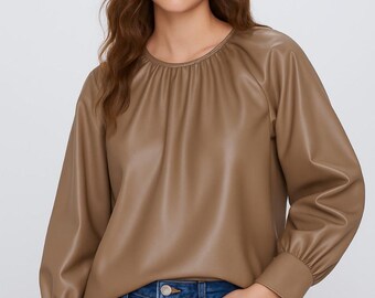 Op de afbeelding: Een bruine top met lange mouwen, een ronde halslijn en gerimpelde details. De top is gemaakt van een glad, leerachtig materiaal. Het model draagt een blauwe jeans.