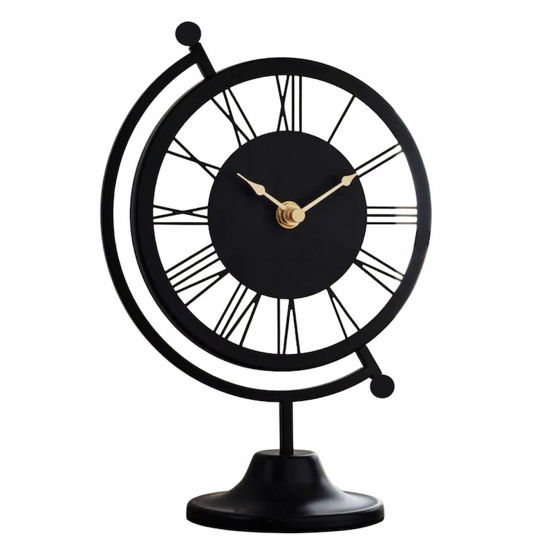 Black metal desk clock in a globe design. The clock features a black face with gold hands and Roman numerals. The clock is supported by a black base and a circular frame. A decorative accent for a home or office.