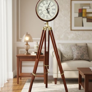 May include: A vintage-style floor clock with a round face and Roman numerals. The clock is mounted on a dark brown wooden tripod stand with brass accents. The clock's face is cream-colored with black hands.