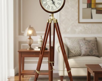 Op de afbeelding: Een vloerklok in vintage-stijl met een ronde wijzerplaat en Romeinse cijfers. De klok is gemonteerd op een donkerbruin houten statief met messing accenten. De wijzerplaat van de klok is crèmekleurig met zwarte wijzers.