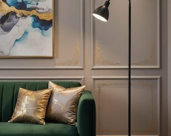 May include: A contemporary black floor lamp with a curved arm and circular base lights a living room. The lamp is positioned beside a green velvet sofa with gold cushions. An abstract painting in a gold frame hangs on the wall.