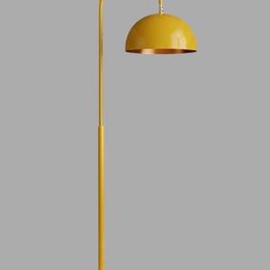 A yellow floor lamp with a curved arm and a dome-shaped shade. The lamp is in a living room with a cream-colored sofa, gold pillows, and a wooden coffee table. The room has cream-colored curtains and a patterned wallpaper.