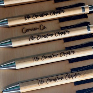 May include: A collection of light brown bamboo pens with silver-toned metal tips and clips. Each pen is engraved with the text The Erenstone Chapter in a black script font. One pen also features the engraved text Carvian Co. above the main title.