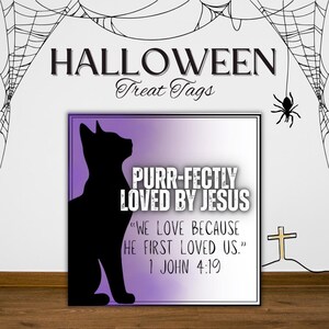 Könnte beinhalten: Halloween-Geschenkanhänger mit einer schwarzen Katzen-Silhouette und dem Text "PURR-FECTLY LOVED BY JESUS". Der Anhänger enthält auch den Bibelvers "WIR LIEBEN, WEIL ER UNS ZUERST GELIEBT HAT." aus 1. Johannes 4:19. Spinnweben und ein Kreuz sind ebenfalls vorhanden.