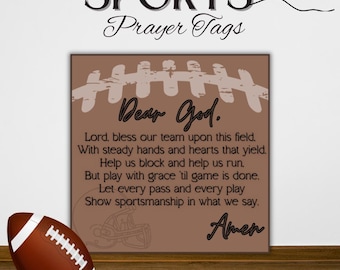May include: A brown football with white stripes rests near a framed sign. The sign features the words "Dear God" and a prayer for a sports team, with the words "SPORTS Prayer Tags" at the top.