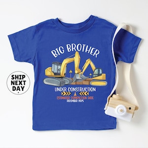 A blue t-shirt with a graphic design depicting construction equipment and the text "BIG BROTHER UNDER CONSTRUCTION ESTIMATED COMPLETION DATE DECEMBER 2035" printed on it.