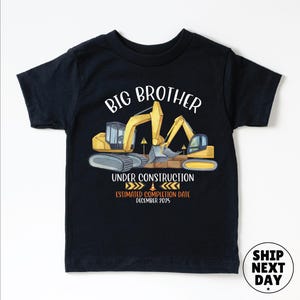 The image is a black t-shirt with a graphic design featuring a yellow excavator and the text "BIG BROTHER UNDER CONSTRUCTION ESTIMATED COMPLIMATION DATE DECEMBER 2023" printed on it.