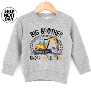 A gray sweatshirt with a graphic design featuring a yellow construction vehicle and the text "BIG BROTHER UNDER CONSTRUCTION" printed on it.